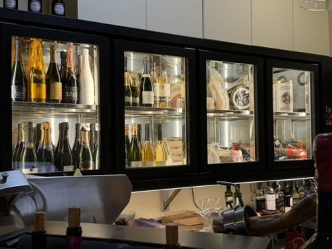 Vitrina de la barra de La Cantina Gastrotaberna con botellas de vino y champagne y quesos